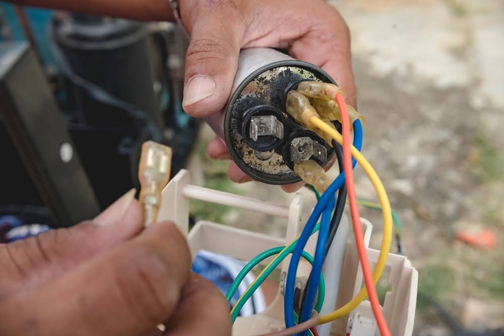 An HVAC technician is replacing a defective AC capacitor.